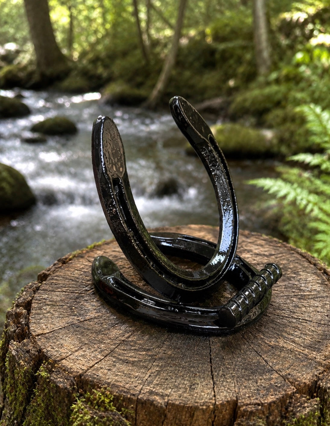 Handmade horseshoe phone and tablet holder - black glossy finish angled view on wood stump